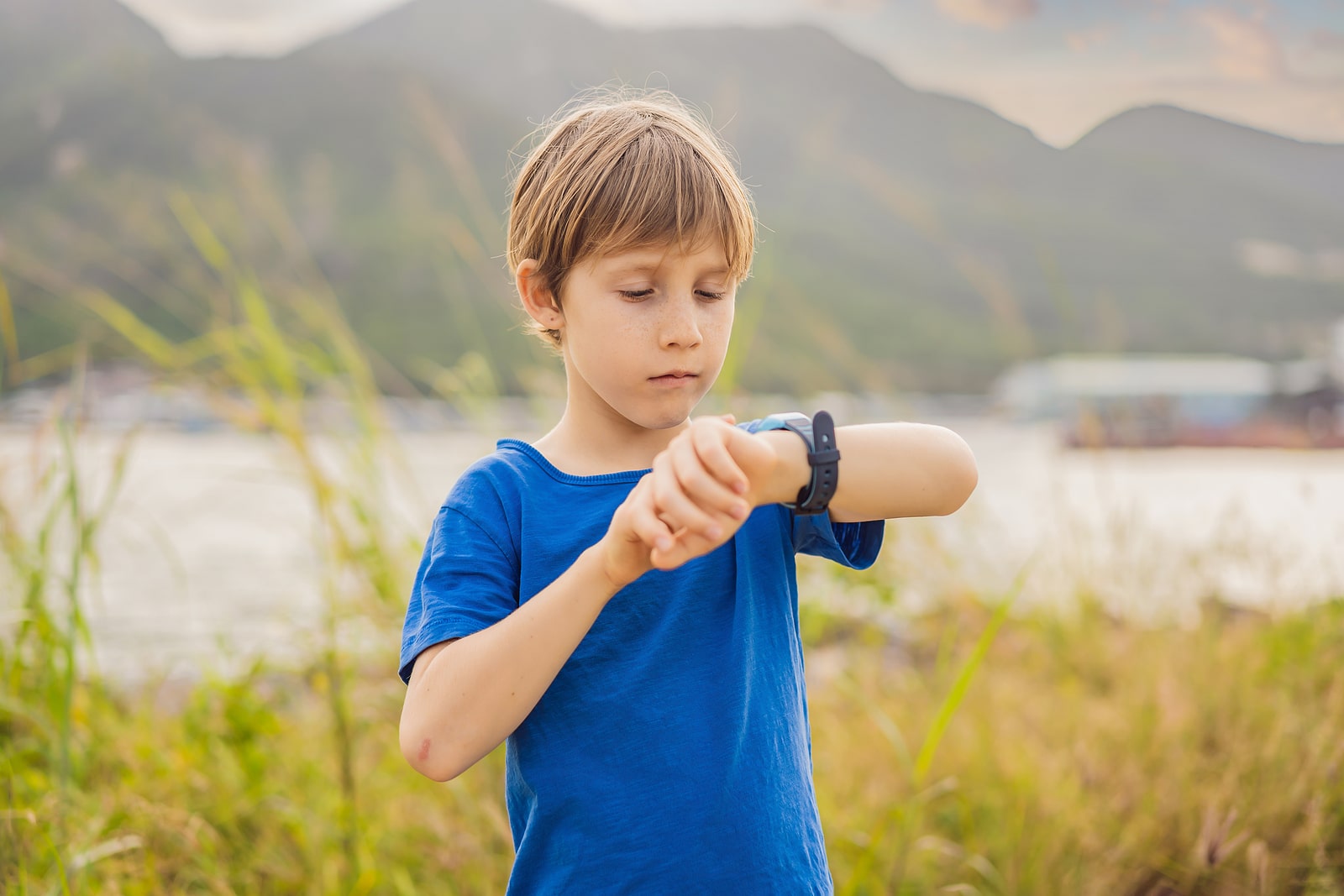 Boy Uses Kids Smart Watch Outdoor Against The Background Of The