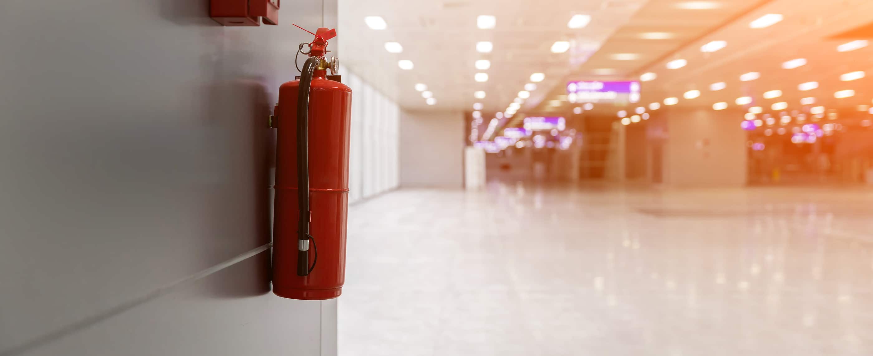 Dry chemical powder fire extinguisher in corridor. Install a fire extinguisher on the wall in building. A red fire-extinguisher hangs on wall .