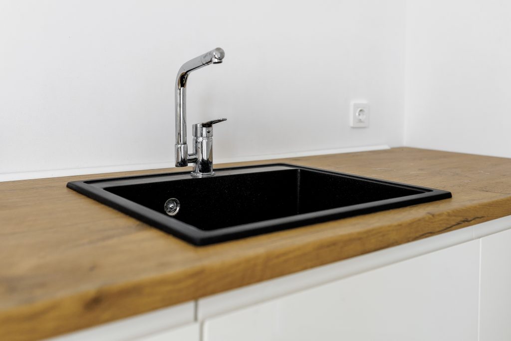 kitchen sink of dark gray stone with chrome faucet in a clean kitchen with a wooden work surface, close up faucet sink