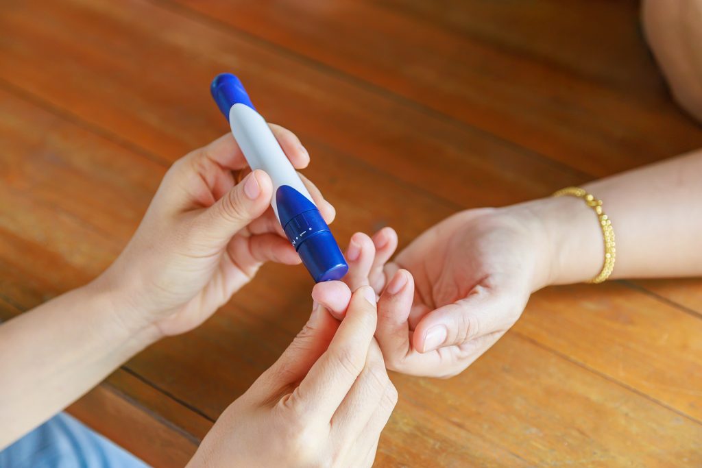 Close up of two woman using lancet on finger to check blood sugar level by Glucose meter using as Medicine