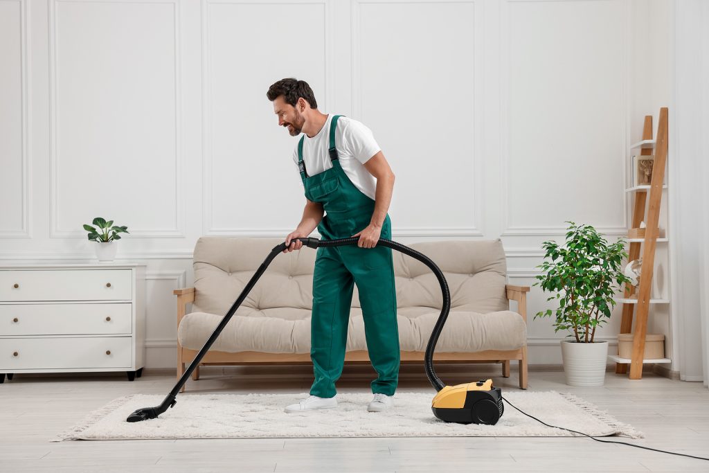 Dry cleaner${2}s employee hoovering carpet with vacuum cleaner in room
