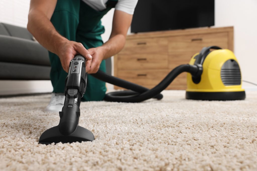 Dry cleaner's employee hoovering carpet with vacuum cleaner indoors, closeup