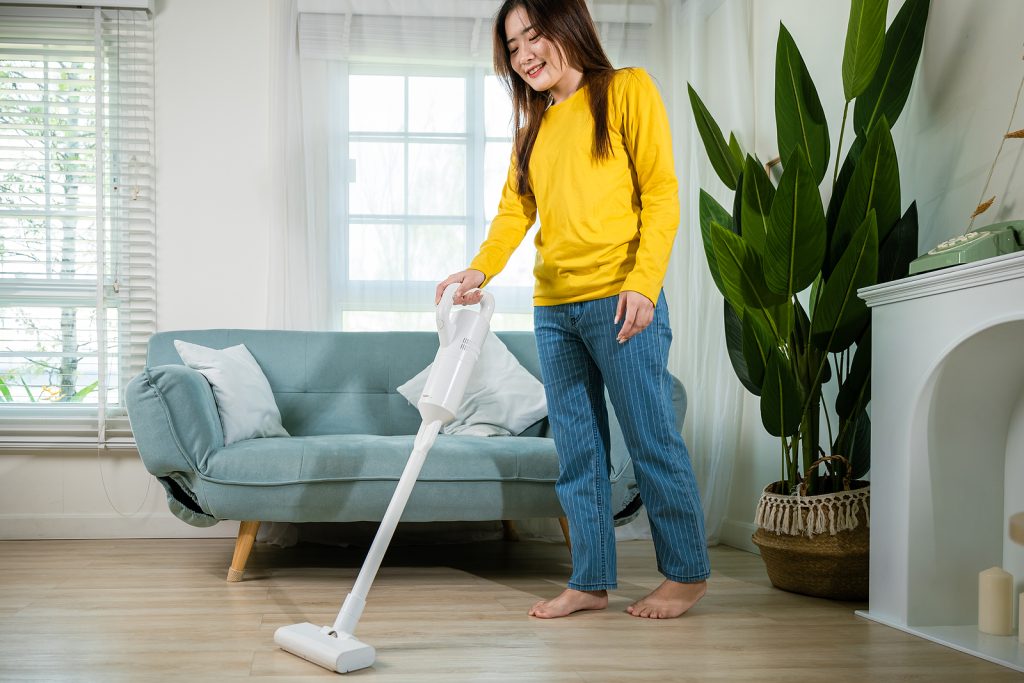 Housewife female dust cleaning floor under sofa or couch furniture with vacuum cleaner