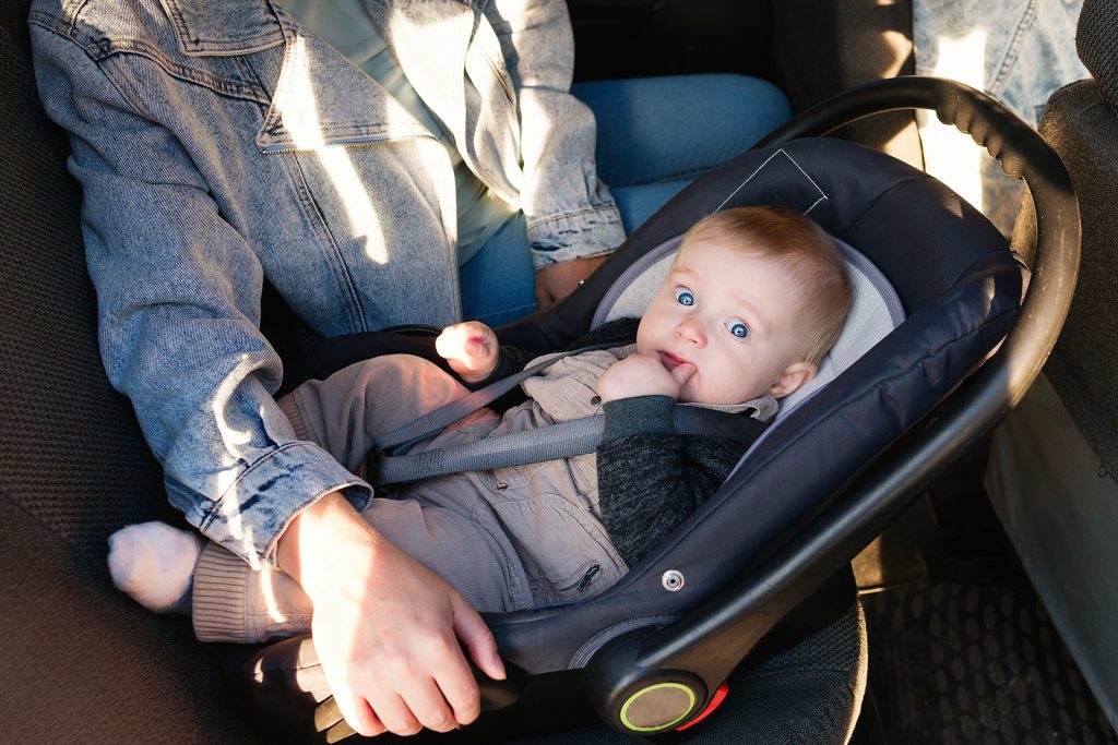 Mother fastening baby to child safety seat inside of car. Kid baby boy in safety car seat.