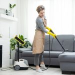 Woman cleaning couch with vacuum cleaner at home