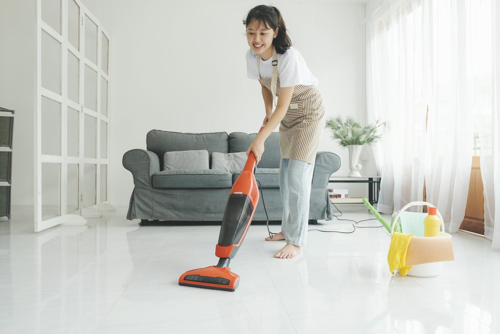 Young woman in casual clothes cleaning floor using vacuum cleaner and cleaning equipments in living room at home.