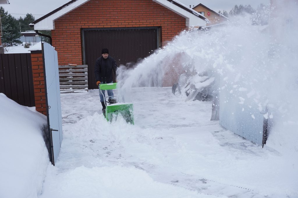 A man cleans snow in the winter in the courtyard of the house, man cleaning snow with a snow blower