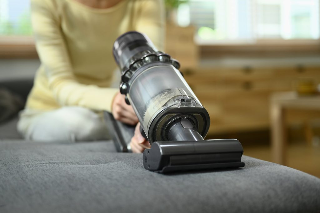 Closeup View Of Young Woman Cleaning Sofa With Cordless Vacuum