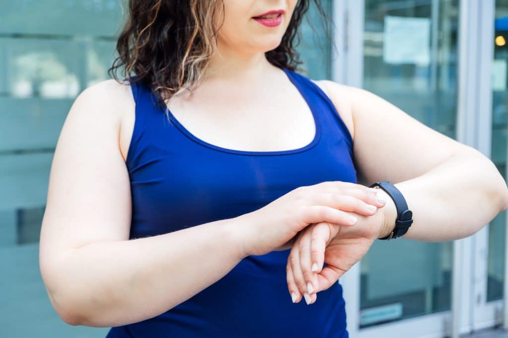 Fitness Wearables, fitness trackers and smartwatches for tracking training performance. Plus size fitness woman looking at hands fitness trackers