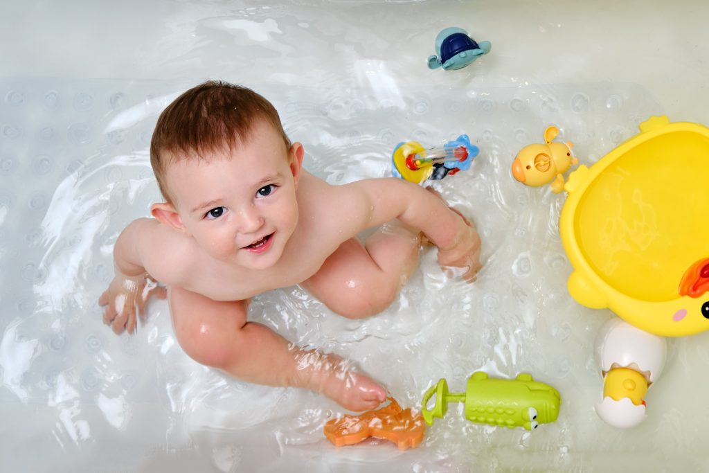 Happy toddler baby boy is playing with toys in the bathtub. A smiling child plays in the water of a home bathroom