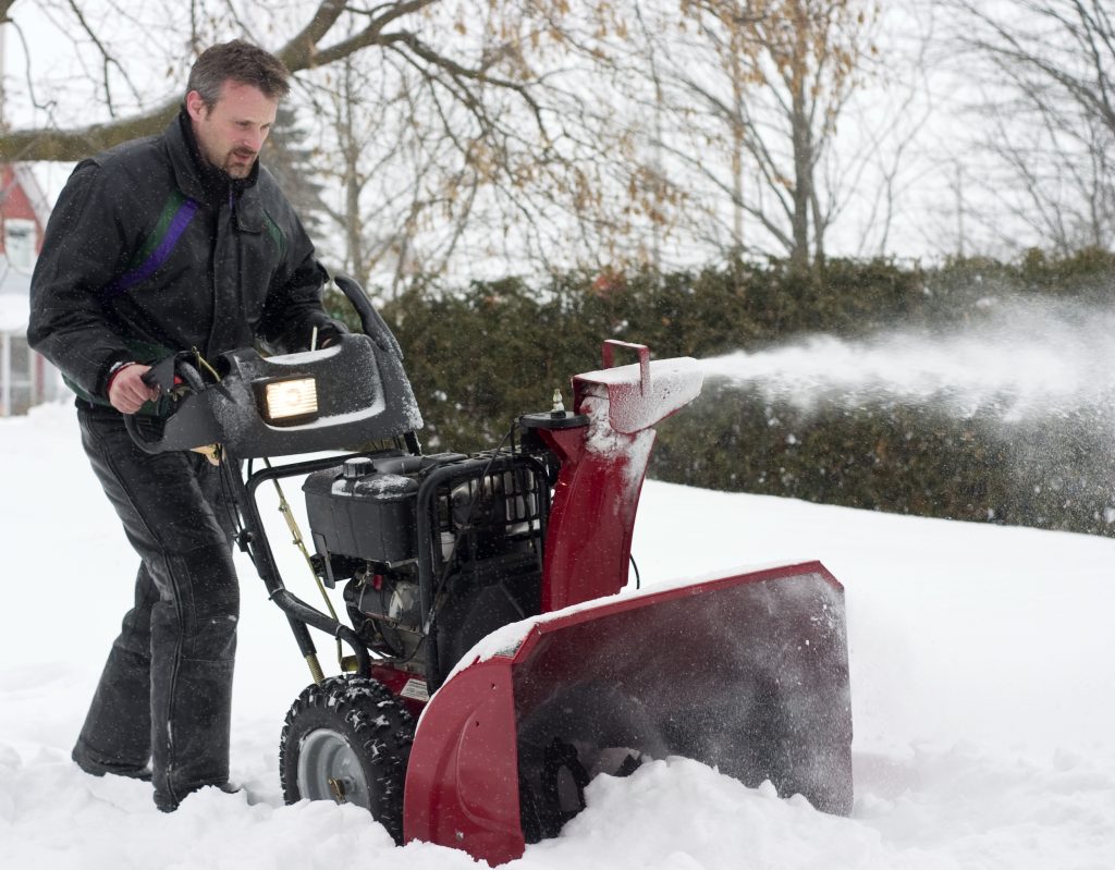man operating snow blower in winter during a snow storm
