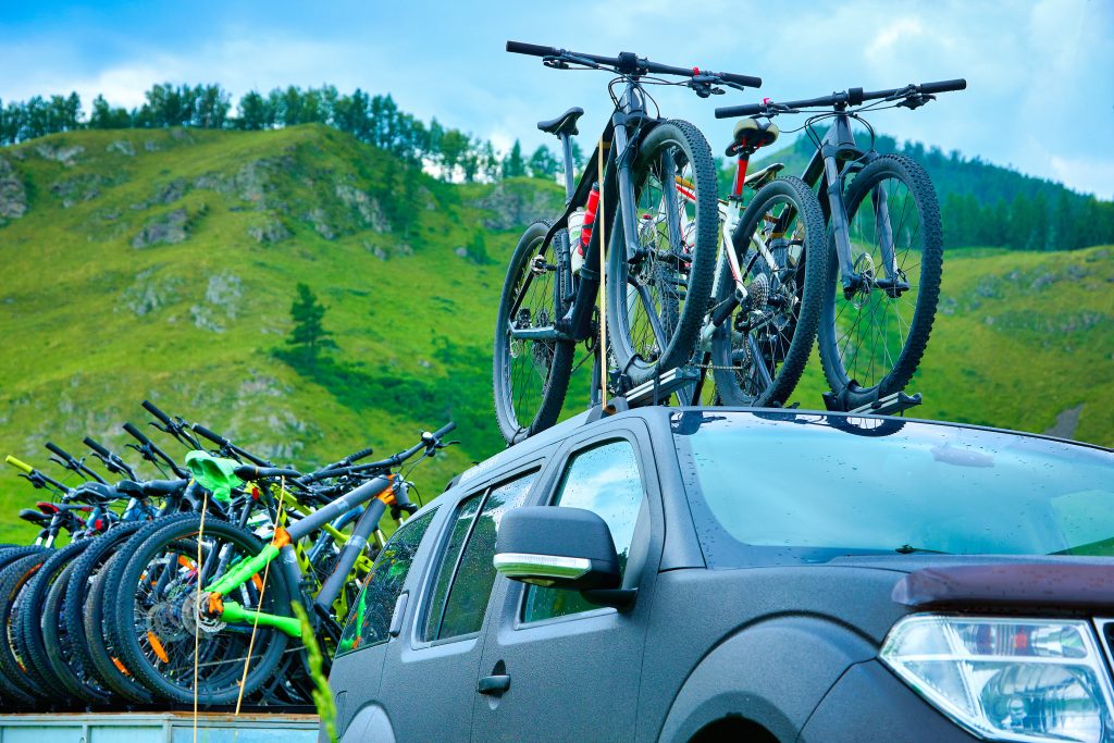 On the roof of the SUV are fixed for transportation several sports bicycles. On a trailer, a off-road vehicle carries fixed mountain bikes for tourists
