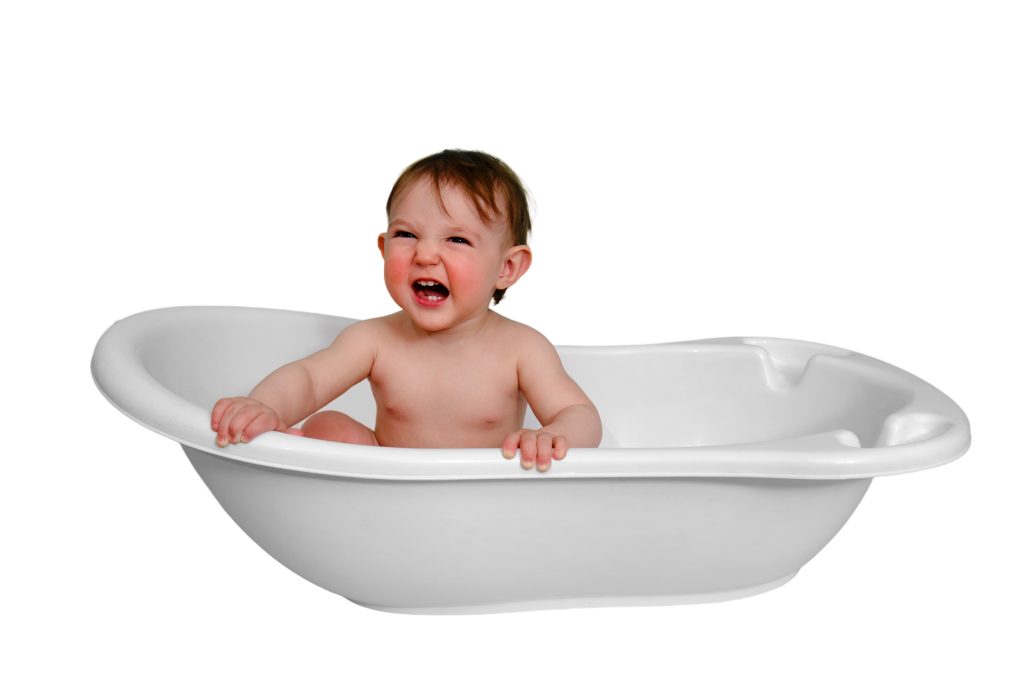 Shouting baby toddler boy is sitting in a bathtub, isolated on white background. Screaming child at the age of one year