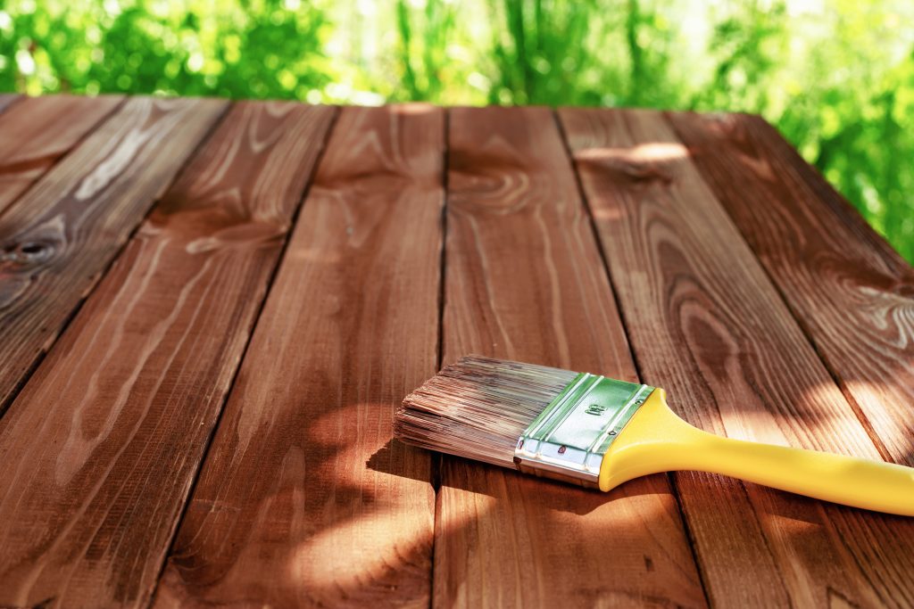 Wood staining diy. Brush. Painting wooden patio deck with protective brown oak varnish. Outdoor decking works. Copy space